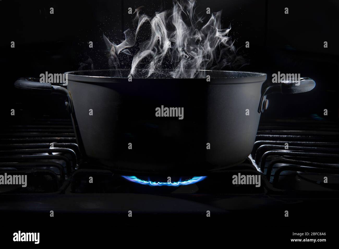 Pentola di cottura sul fuoco di stufa con il cibo all'interno in una cucina scura e uno sfondo nero con vapore che esce dal pentola di cottura, luce chiave bassa. Foto Stock
