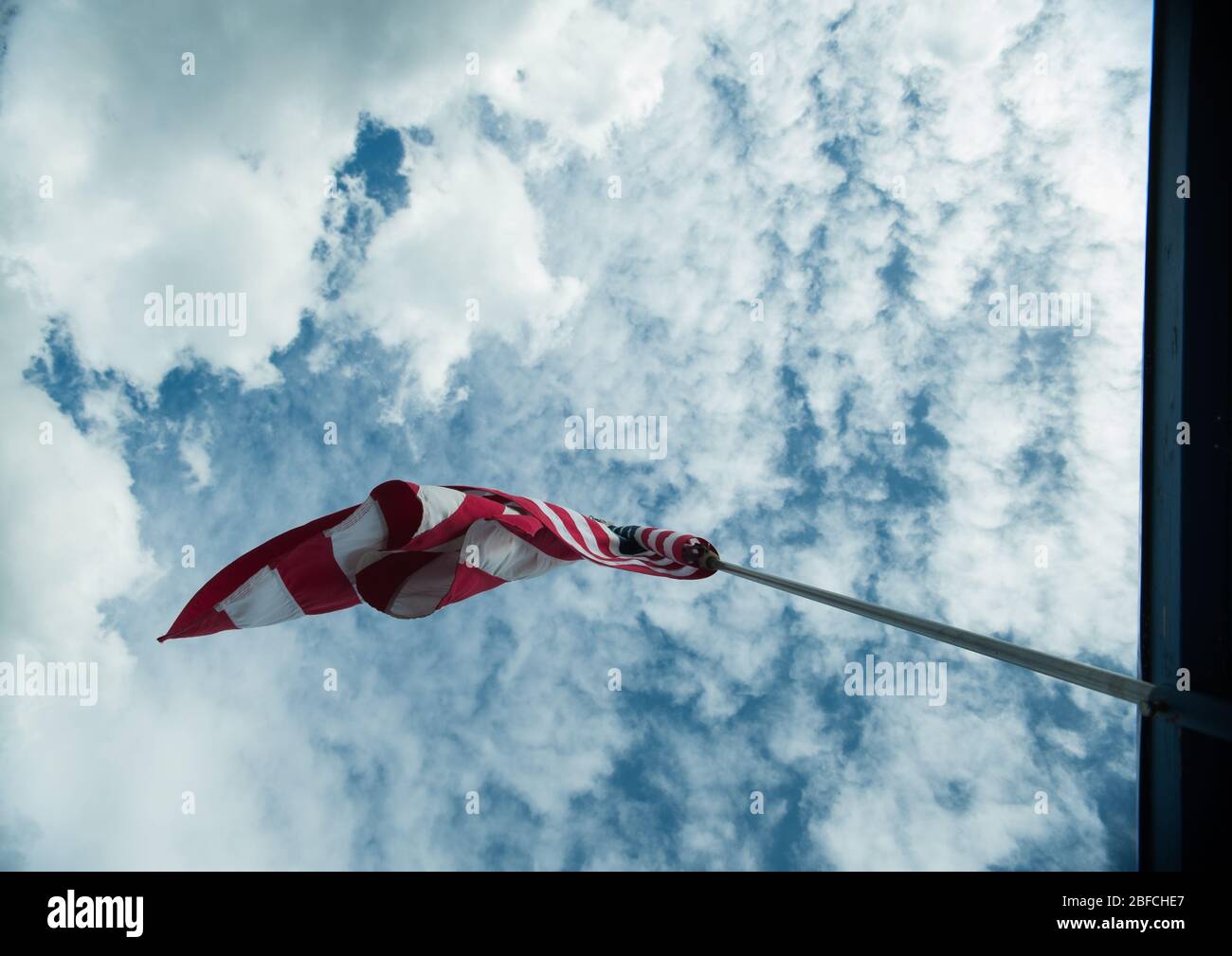 Bandiera americana degli Stati Uniti soffiando nel vento alto sul flagpole torreggiando sopra lo sfondo di cielo blu nuvoloso simbolo di stelle e strisce americane Foto Stock