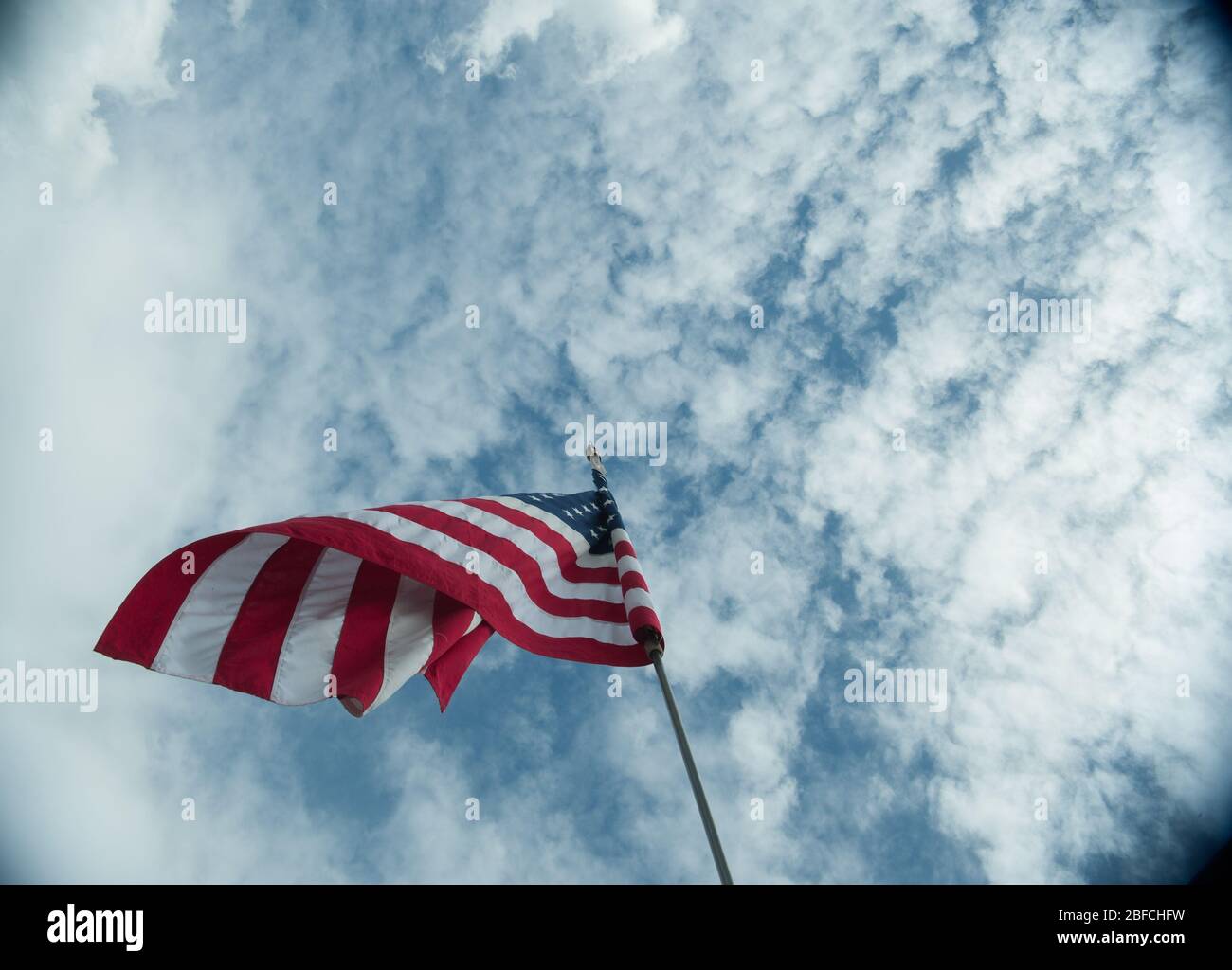 Bandiera americana degli Stati Uniti soffiando nel vento alto sul flagpole torreggiando sopra lo sfondo di cielo blu nuvoloso simbolo di stelle e strisce americane Foto Stock