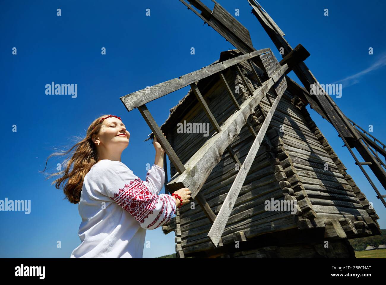 Bella ragazza ucraina vicino in legno mulino a vento in bianco maglietta etnica a livello nazionale museo di architettura in Pirogovo. A Kiev, Ucraina Foto Stock