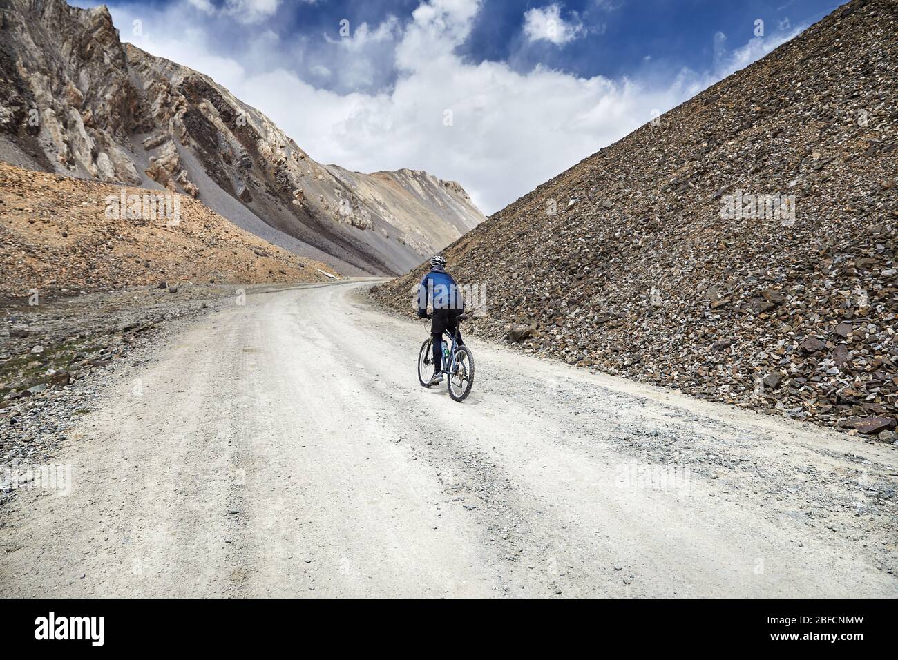 Uomo in mountain bike sulla strada in alta montagna contro il cielo blu sullo sfondo. Foto Stock