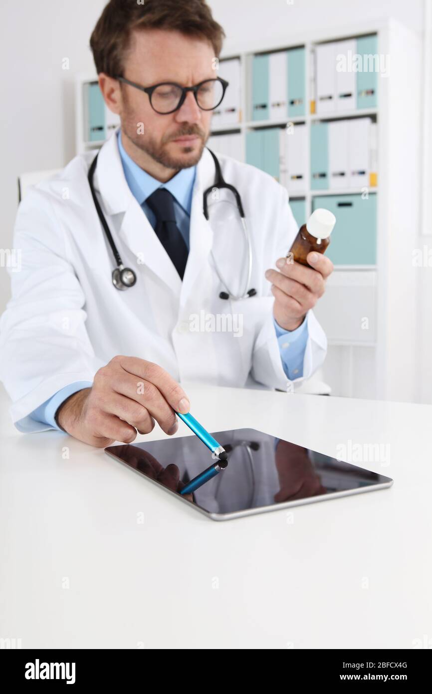 medico che scrive prescrizione in ufficio medico con le droghe touch tablet digitale sulla scrivania Foto Stock