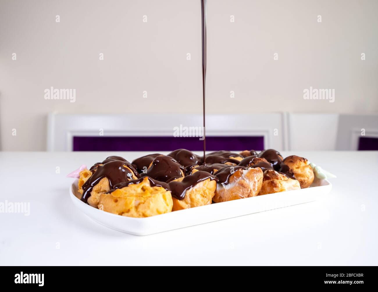 Cioccolato Profiterolo. Dessert dolce su piatto bianco. Profiteroles fatti in casa con crema e salsa al cioccolato. Foto Stock