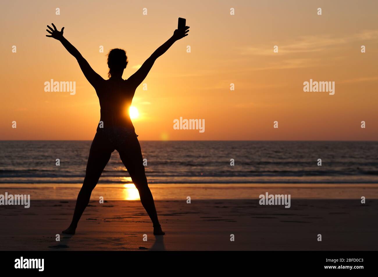 Una giovane donna felice che celebra la fine del blocco, sulla spiaggia al tramonto dopo la pandemia coronavirus Foto Stock