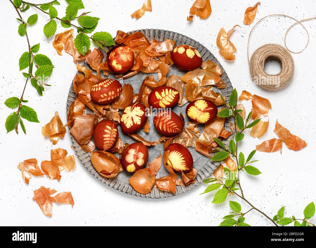 Uova di Pasqua tinte con bucce di cipolla e modello di foglie fresche di piante in una piastra metallica rustica. Concetto fai da te. Vista dall'alto. Foto Stock