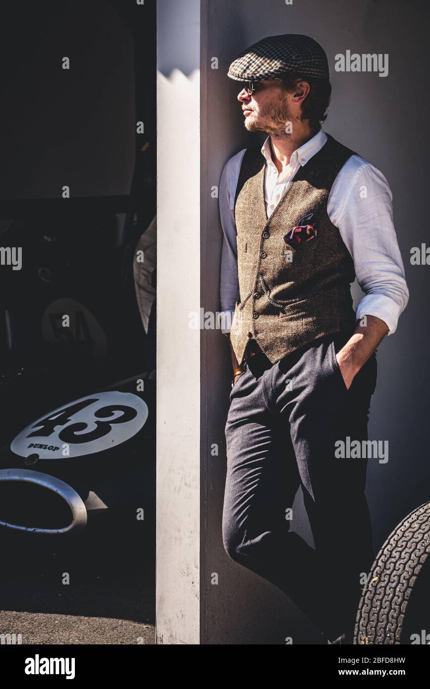 Uomo in posa in cappello piatto e corpetto in tweed accanto al naso di una vettura Grand Prix d'epoca a Goodwood Revival, Goodwood Motor Racing Circuit Foto Stock