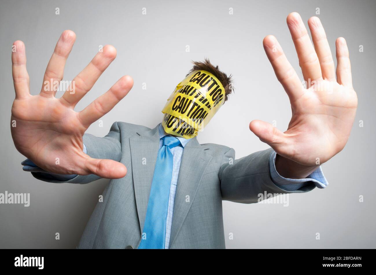 Uomo d'affari divertente con faccia coperta di nastro di attenzione giallo e nero che tiene fuori le mani per la sicurezza Foto Stock