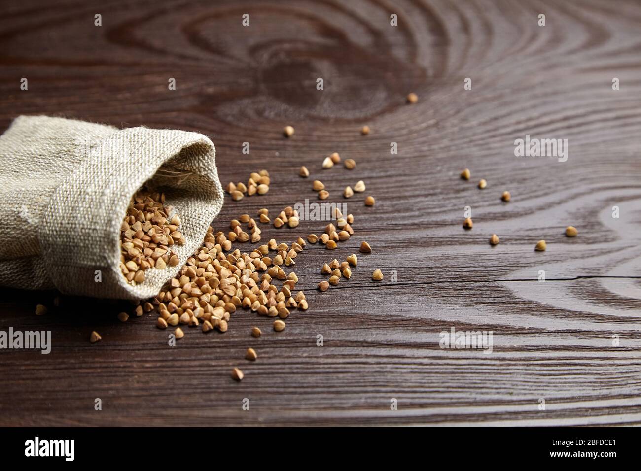Semole di grano saraceno (semi di colmi) in borsa di tela. Grano saraceno intero sparso su sfondo di legno con spazio copia, fuoco selettivo Foto Stock