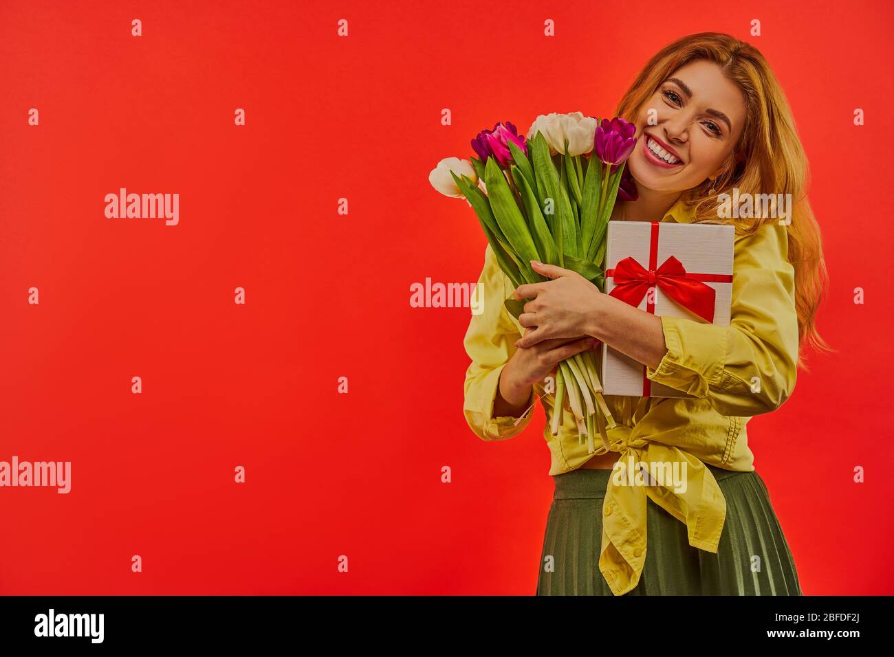 Belle donne con sorriso in una blusa e una gonna con un bouquet di fiori e presente in mano. Foto Stock