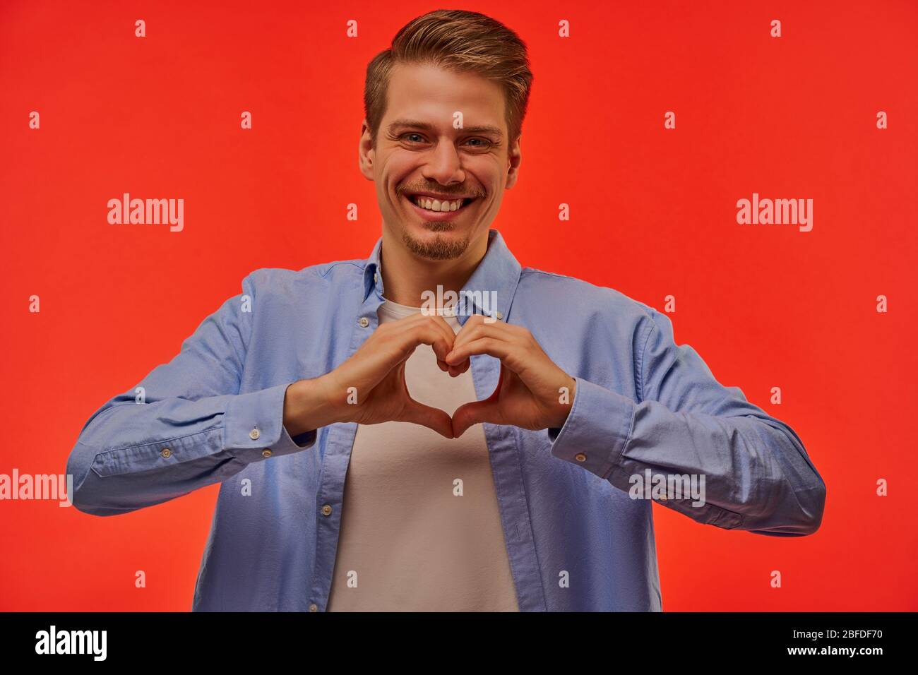 L'uomo di felicità in una camicia blu mostra un simbolo del cuore. Foto Stock