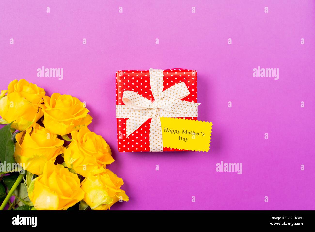 Confezione regalo rossa con biglietto di auguri e testo Happy Woman's Day, rose gialle su sfondo viola. Spazio libero. Spazio di copia per il testo. Giorno della madre Foto Stock