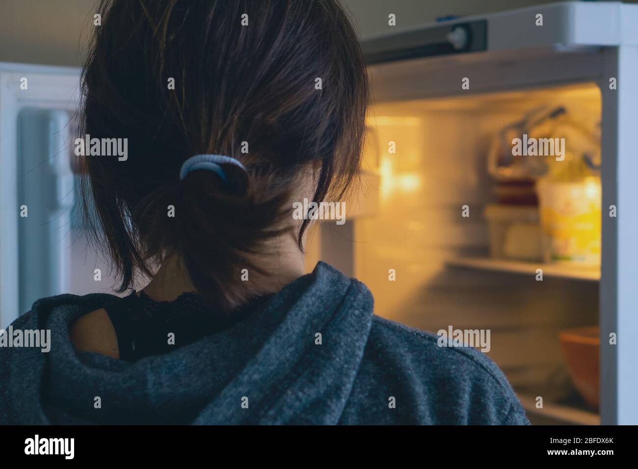 Vista posteriore di una donna che guarda in frigorifero aperto a casa o cucina. Foto Stock