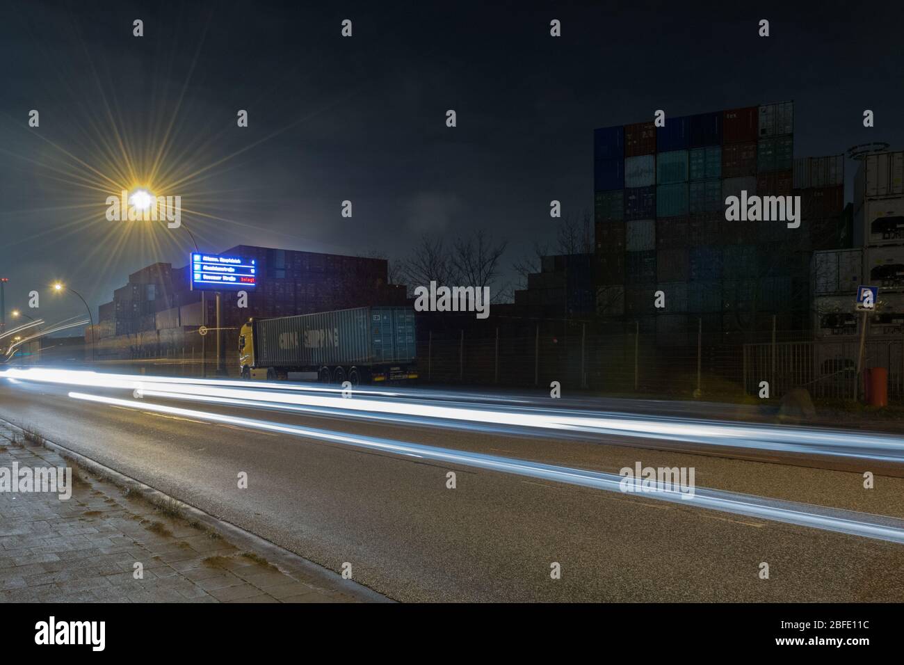 Area container del porto di Amburgo di notte - foto a lunga esposizione con le auto che passano e i loro fasci di luce Foto Stock