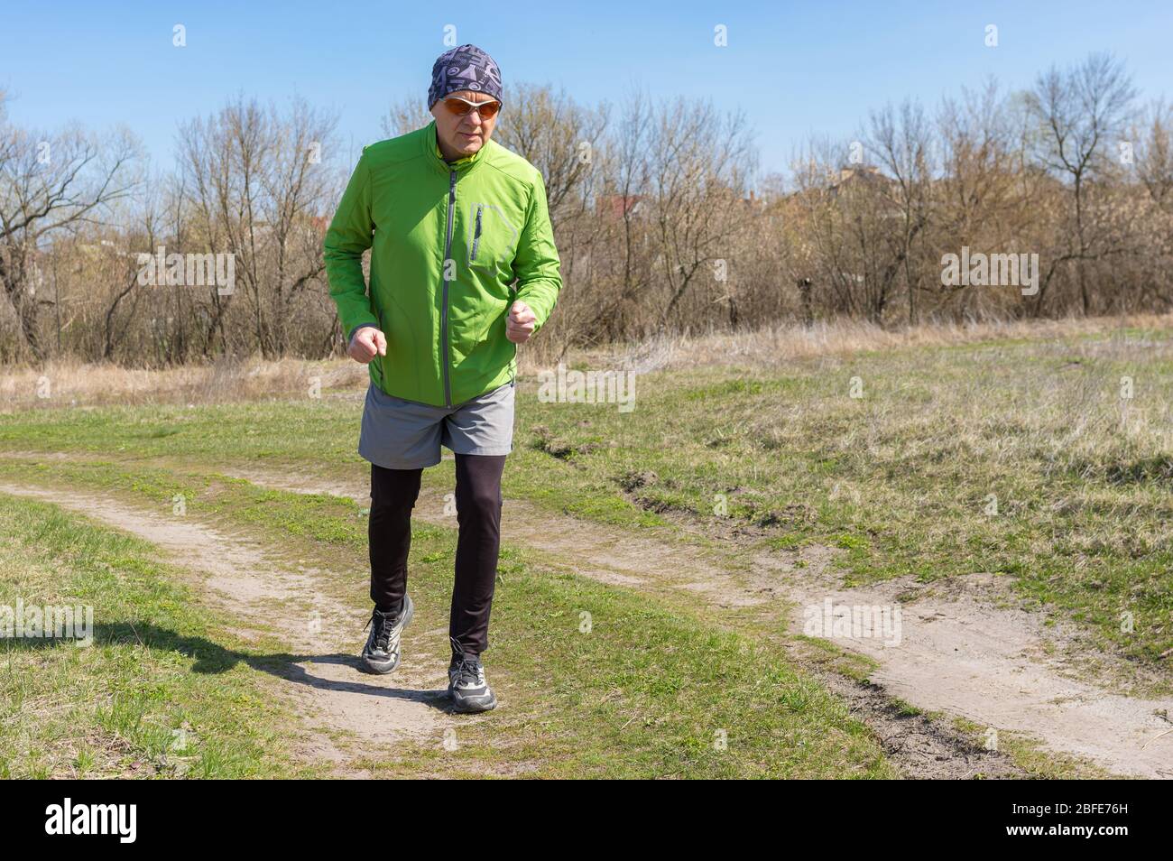 Uomo senior caucasico che corre solitario su una strada di campagna all'inizio della stagione primaverile Foto Stock