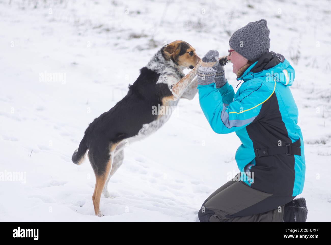 Donna matura felice che gioca con cane di razza mista nero su un terreno coperto di neve durante la stagione invernale Foto Stock
