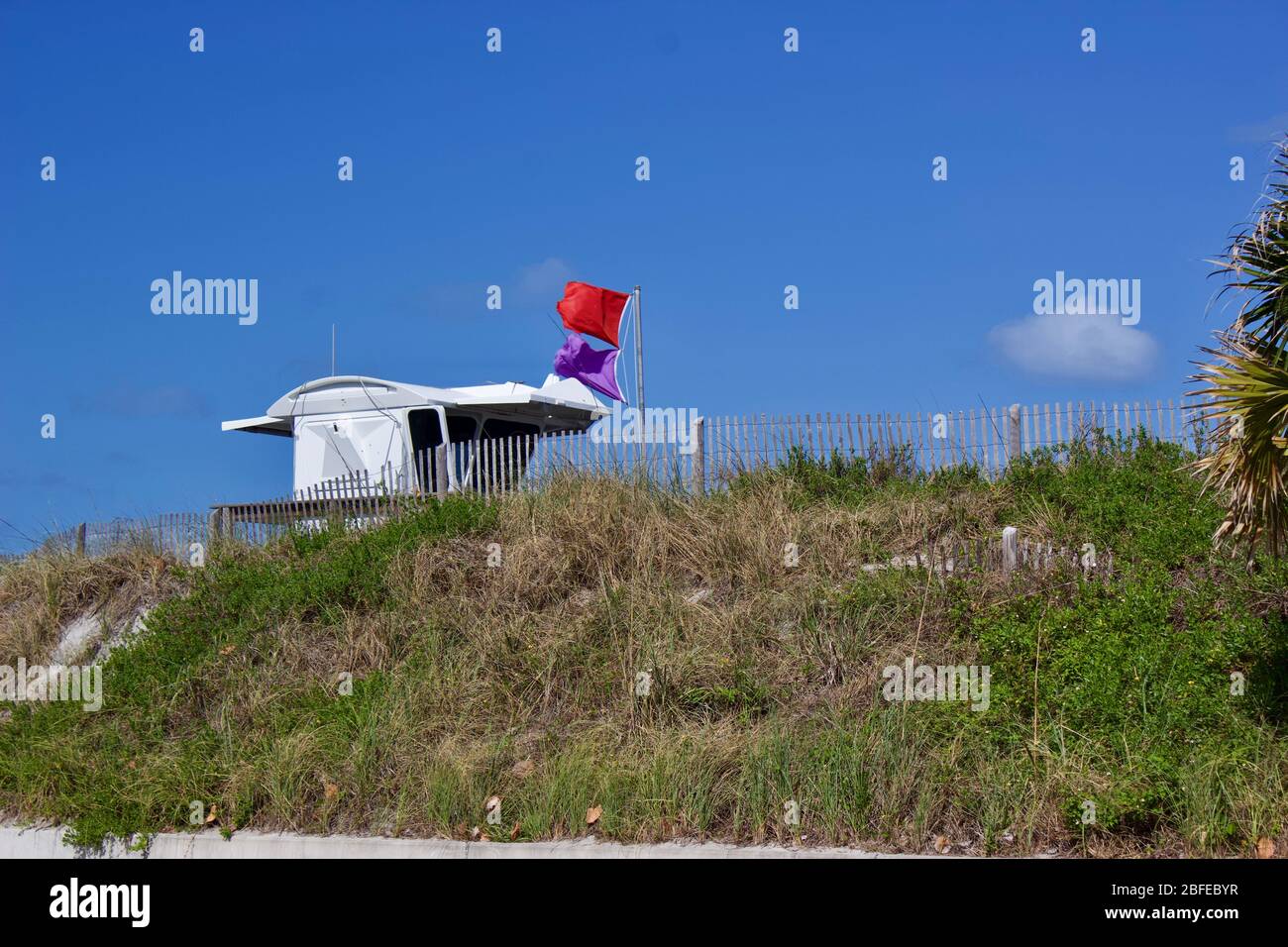 Supporto per bagnino con bandierine di avvertenza che indicano un pericolo derivante da una pericolosa vita marina e un pericolo derivante dal surf, sul punto più alto delle dune di sabbia e recinzioni di sabbia. Foto Stock