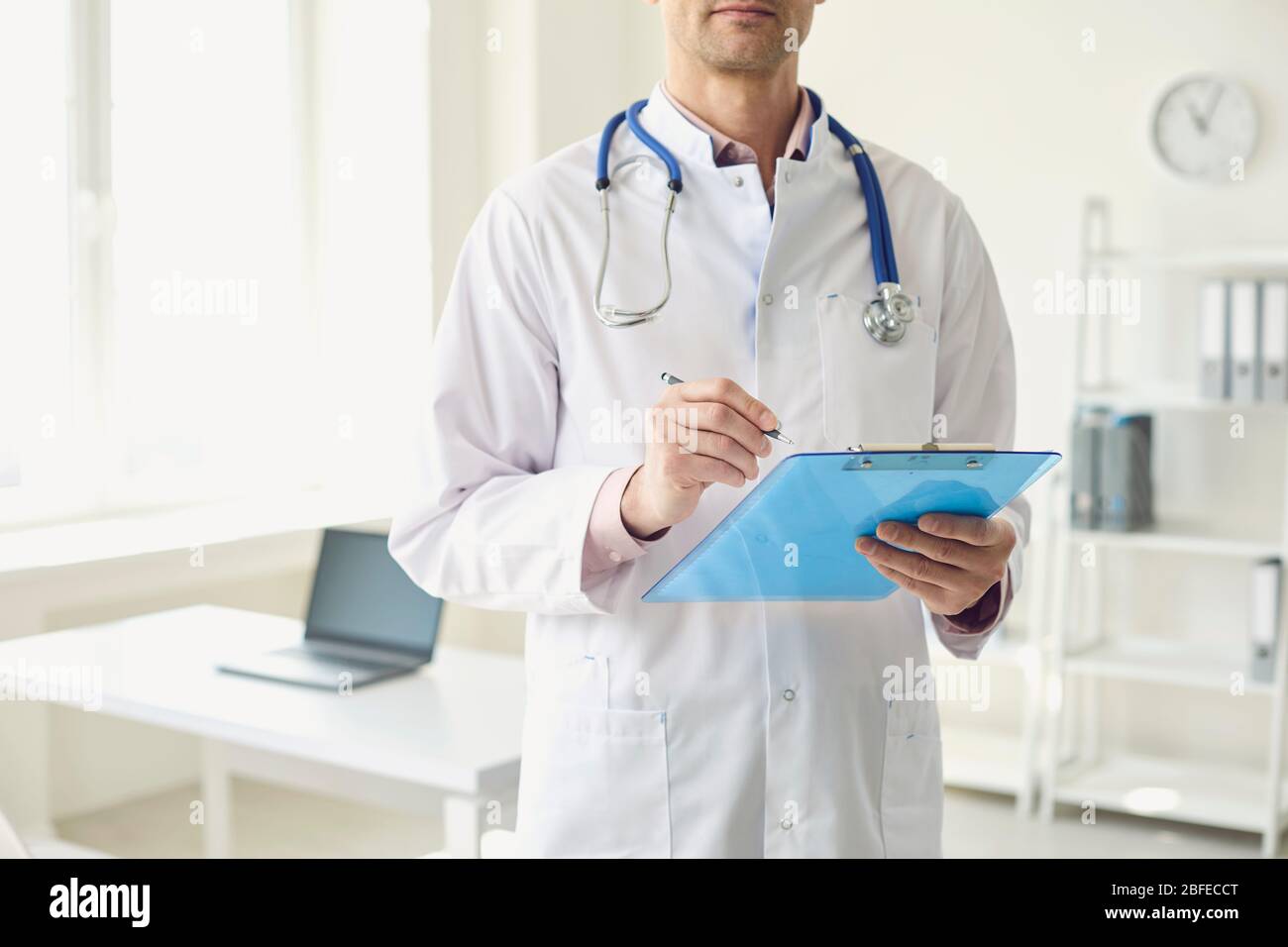 Il primo piano di un medico scrive una prescrizione in un clipboard per trattare un paziente mentre si trova in piedi all'ufficio di una clinica medica. Foto Stock