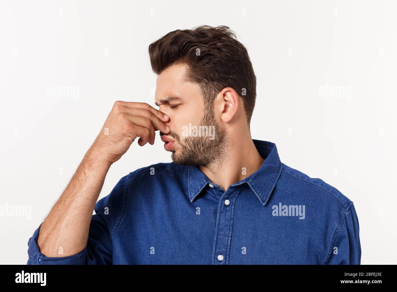 Uomo che tiene il naso contro un cattivo odore isolato su sfondo grigio. Foto Stock