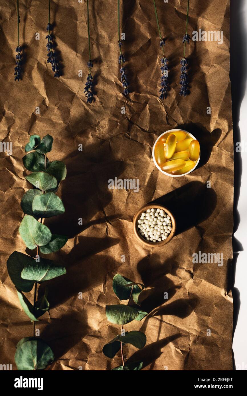 Vista dall'alto sulle capsule di olio di pesce e le palle omeopatiche giacciono su carta da imballaggio stropicciata. Circondato da rametti di eucalipto e lavanda. Foto Stock