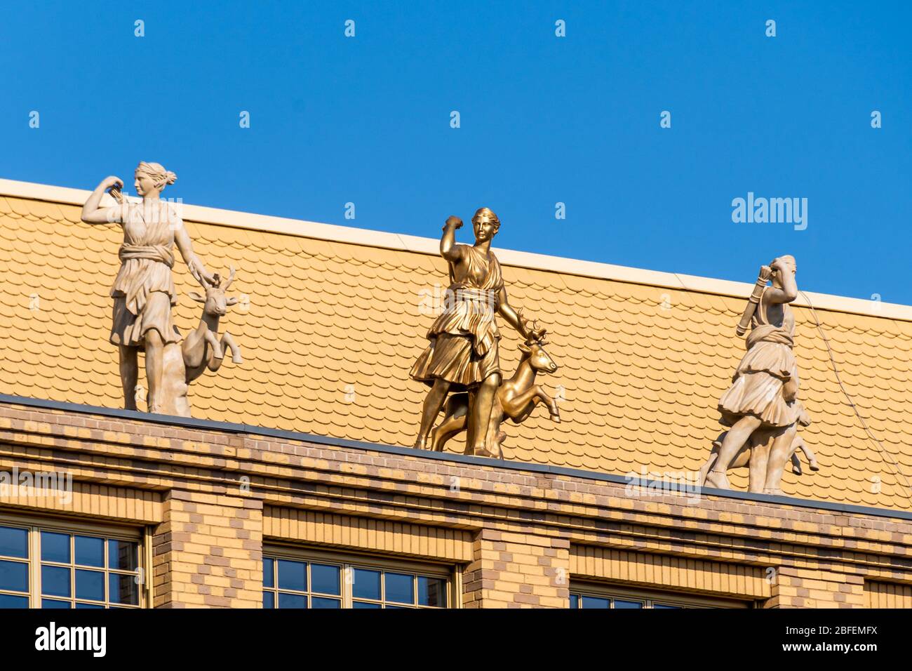 Statua dorata di Diana oltre a statue di marmo sulla parte superiore della facciata in mattoni gialli con motivi Foto Stock