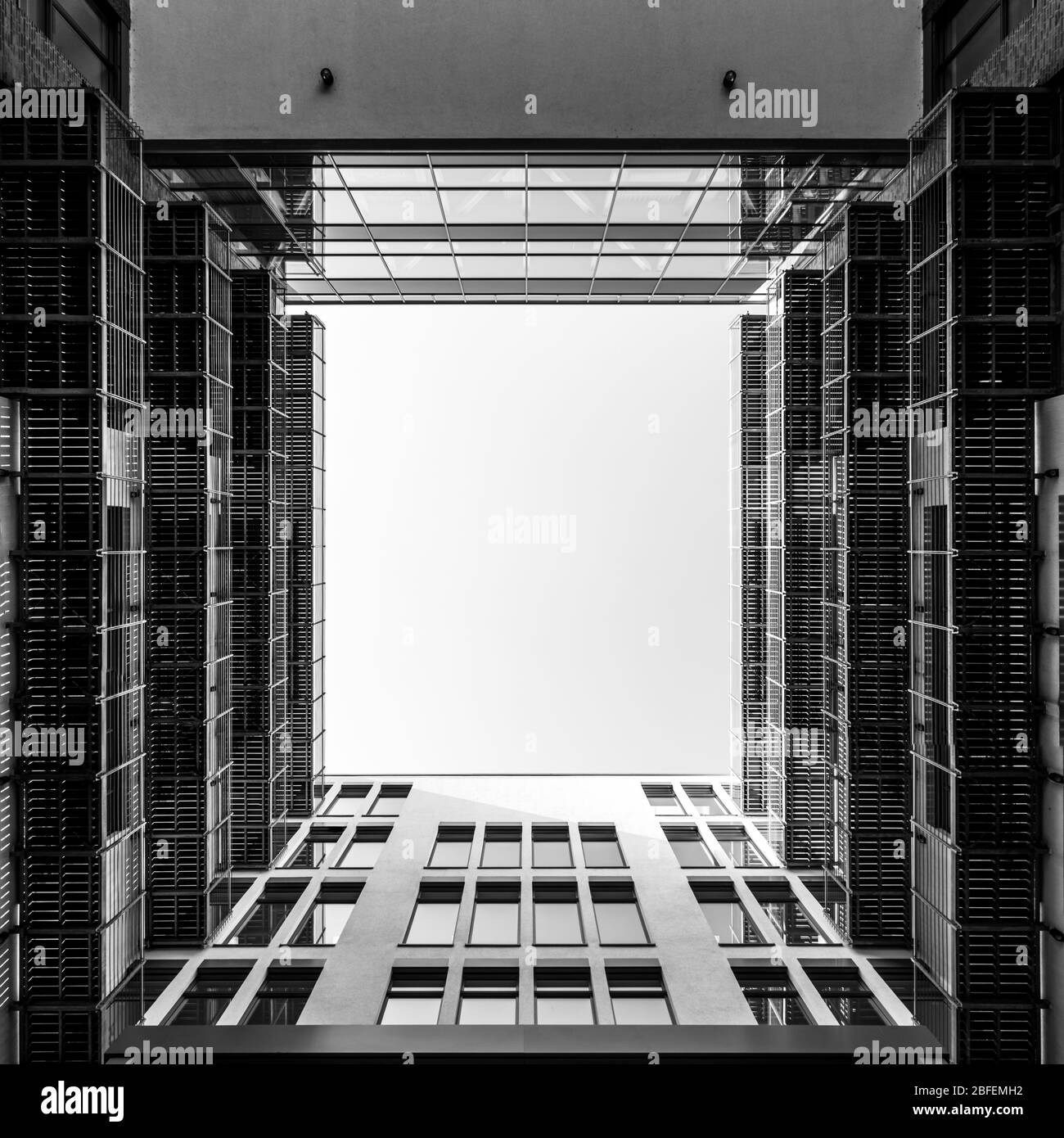 Cortile interno di un moderno edificio di uffici che guarda verso l'alto attraverso la piazza che si apre nel cielo in bianco e nero Foto Stock