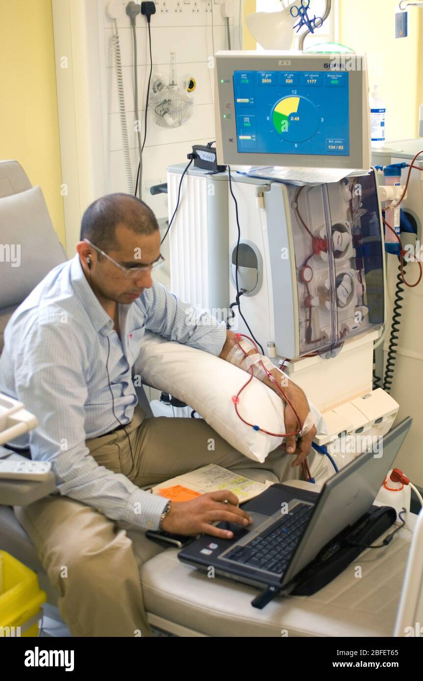 Un dirigente aziendale al lavoro sul suo computer mentre è collegato ad una macchina per emodialisi che sta pulendo il suo sangue di rifiuti di fluidi renali e a. Foto Stock