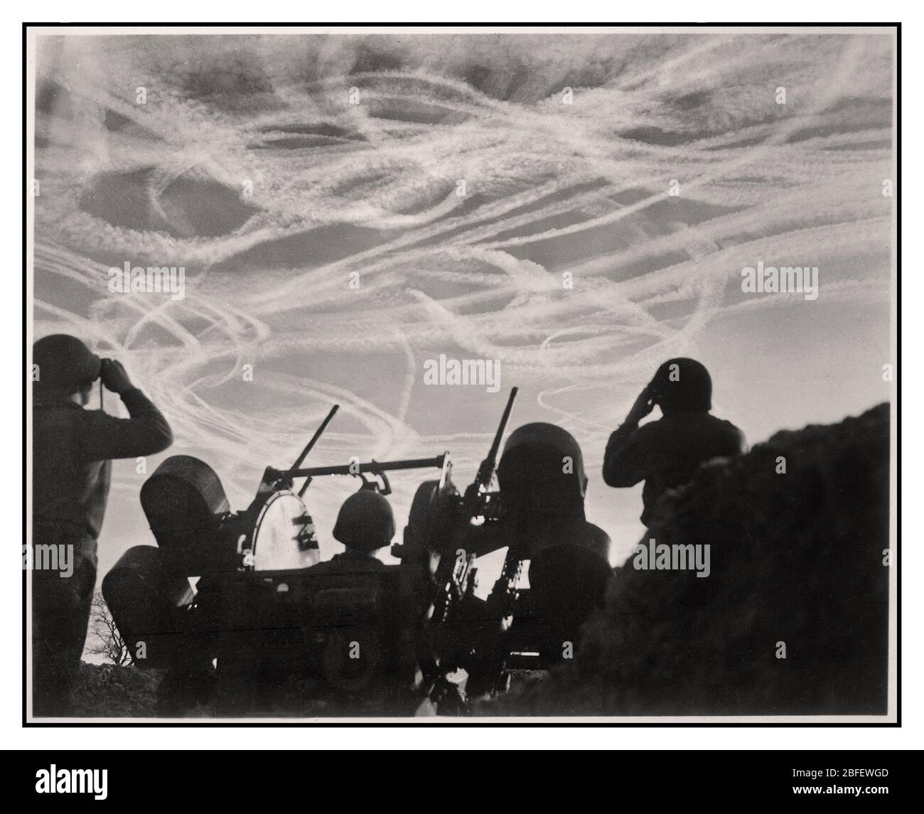 La BATTAGLIA del CANE aereo DI Vapor Trails in Germania durante la seconda Guerra Mondiale immagine GIS di una batteria M-51 Anti-Aircraft che guarda il combattimento aereo, si staglia contro il cielo tedesco cosparso di piste di vapore di dogfight da aerei alleati e nemici, impegnati nella lotta del cane del giorno di Natale. Vicino a Puffendorf, Germania. I combattimenti dei cani del giorno di Natale hanno cosparso il cielo di sentieri di vapore da aerei Alleati e tedeschi. I soldati di una batteria antiaerea guardano l'azione su Puffendorf, Germania. 25 dicembre 1944. Battaglia della Bulge, guerra mondiale 2. Foto Stock