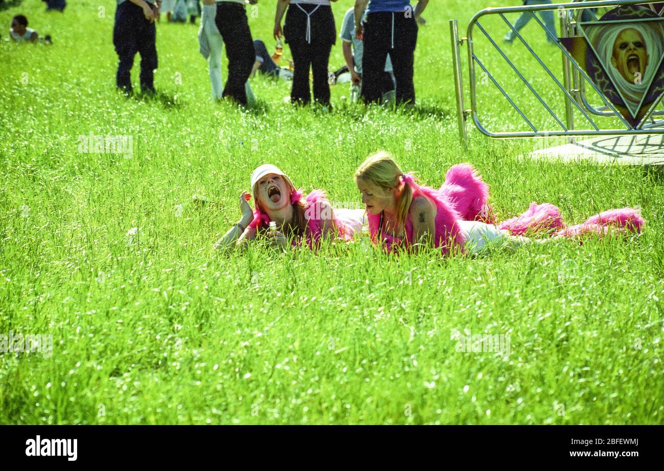 Due ragazze in stivali e gilet di rave lanciò nell'erba al festival di Homeeland, Hampshire, UK, 2002 Foto Stock