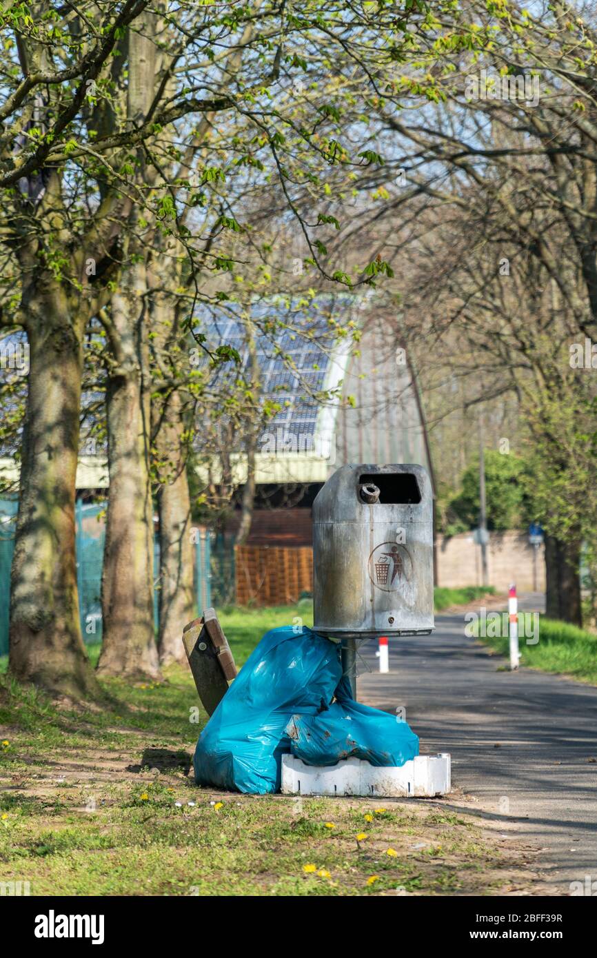 Sacchetti di plastica blu riempiti di immondizia vicino ad un cestino di metallo vuoto possono in un parco pubblico. Inquinamento ambientale, smaltimento illegale dei rifiuti in natura Foto Stock