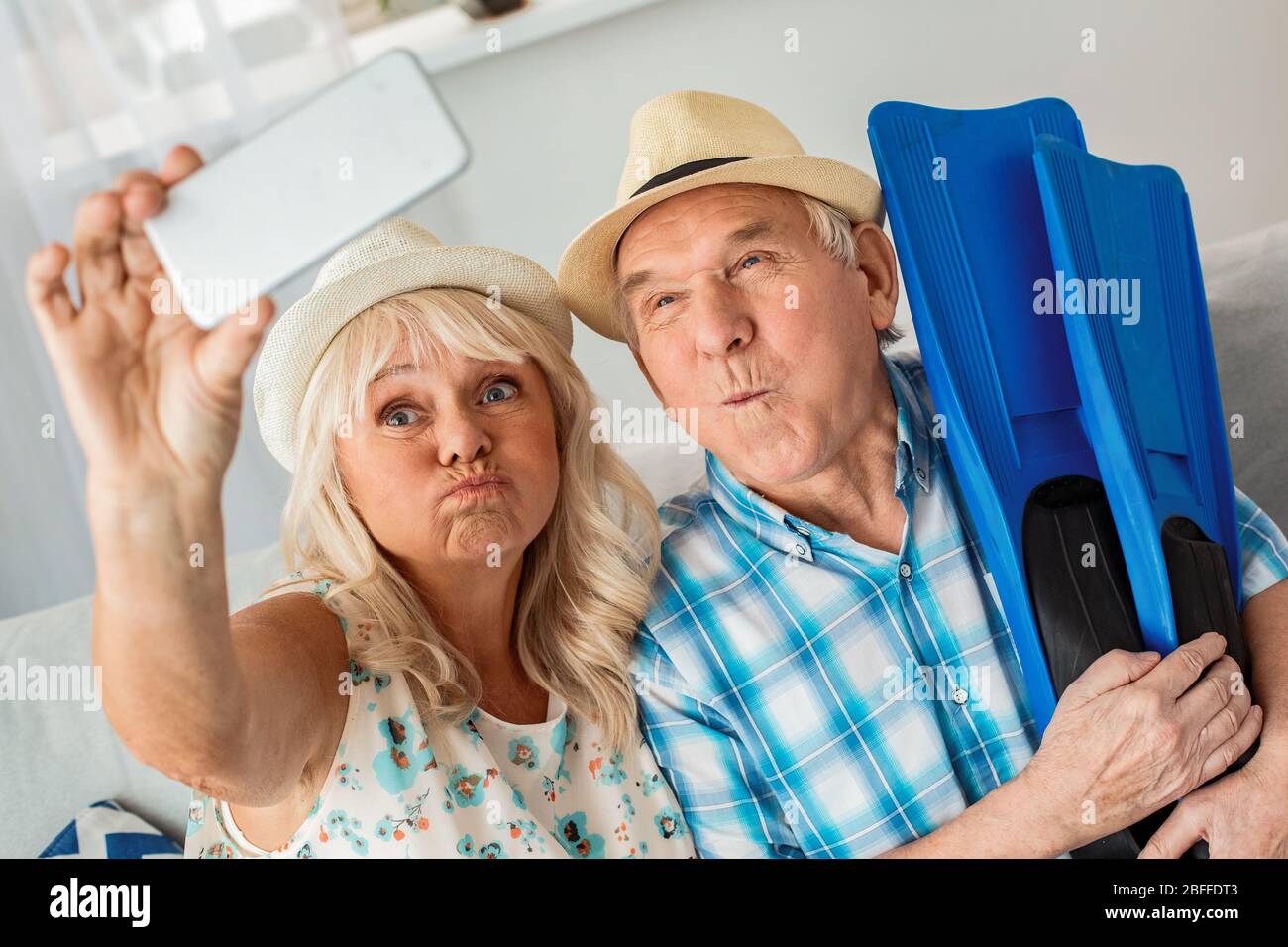 Coppia senior seduta in agenzia di viaggio seduta indossare cappelli marito tenere le pinne mentre moglie scattare foto selfie su smartphone Grimace divertente Foto Stock