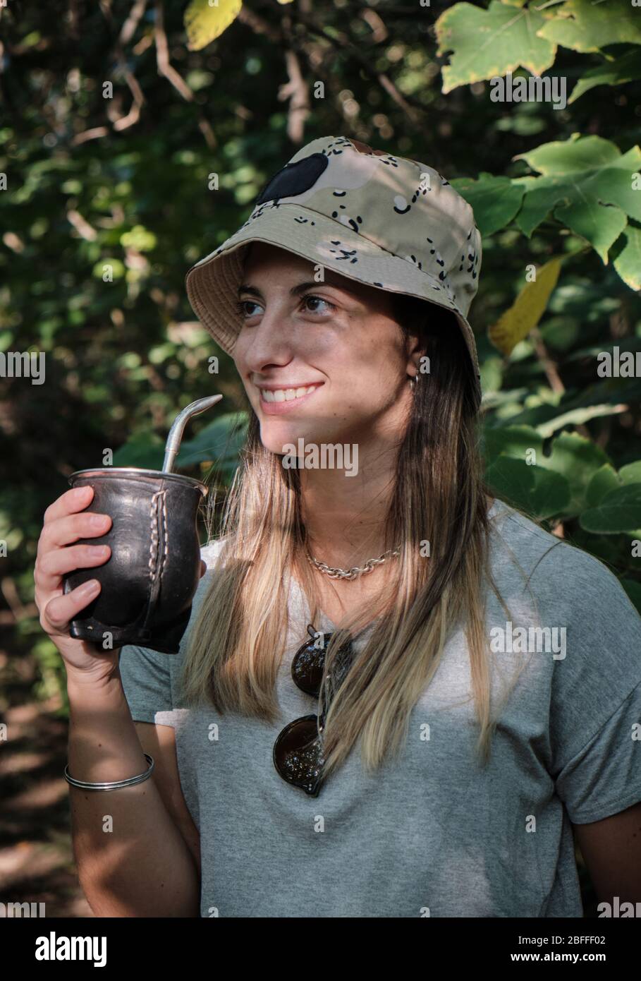 una bella donna modello bere yerba mate infusione mentre si cammina attraverso gli alberi Foto Stock