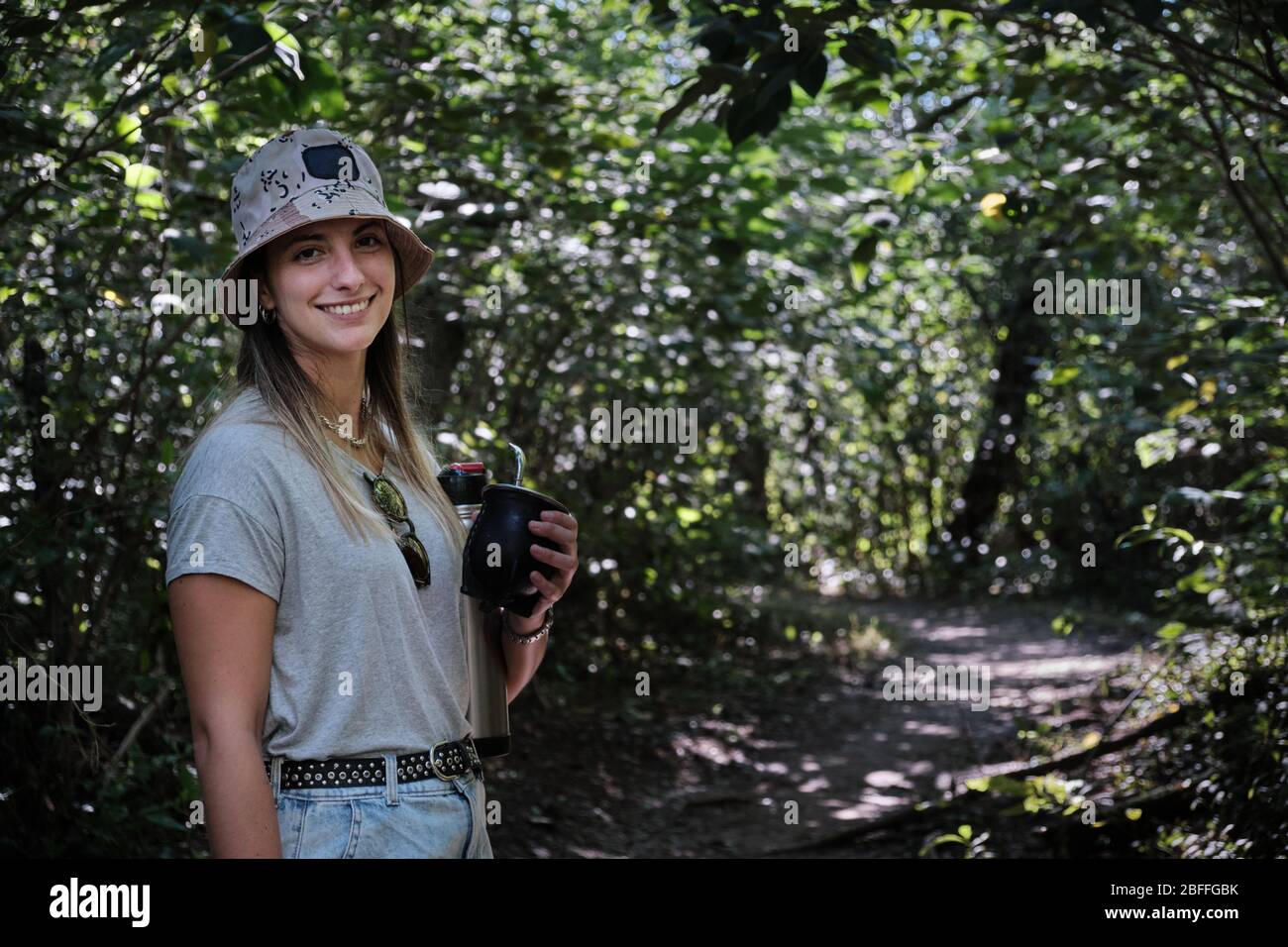 una bella donna modello bere yerba mate infusione mentre si cammina attraverso gli alberi Foto Stock