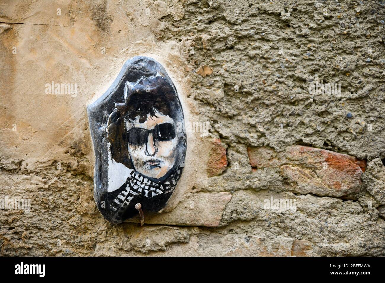 Primo piano di una pietra dipinta a mano con il ritratto di Bob Dylan, cantautore americano, su un vecchio muro, Bussana Vecchia, Imperia, Liguria, Italia Foto Stock
