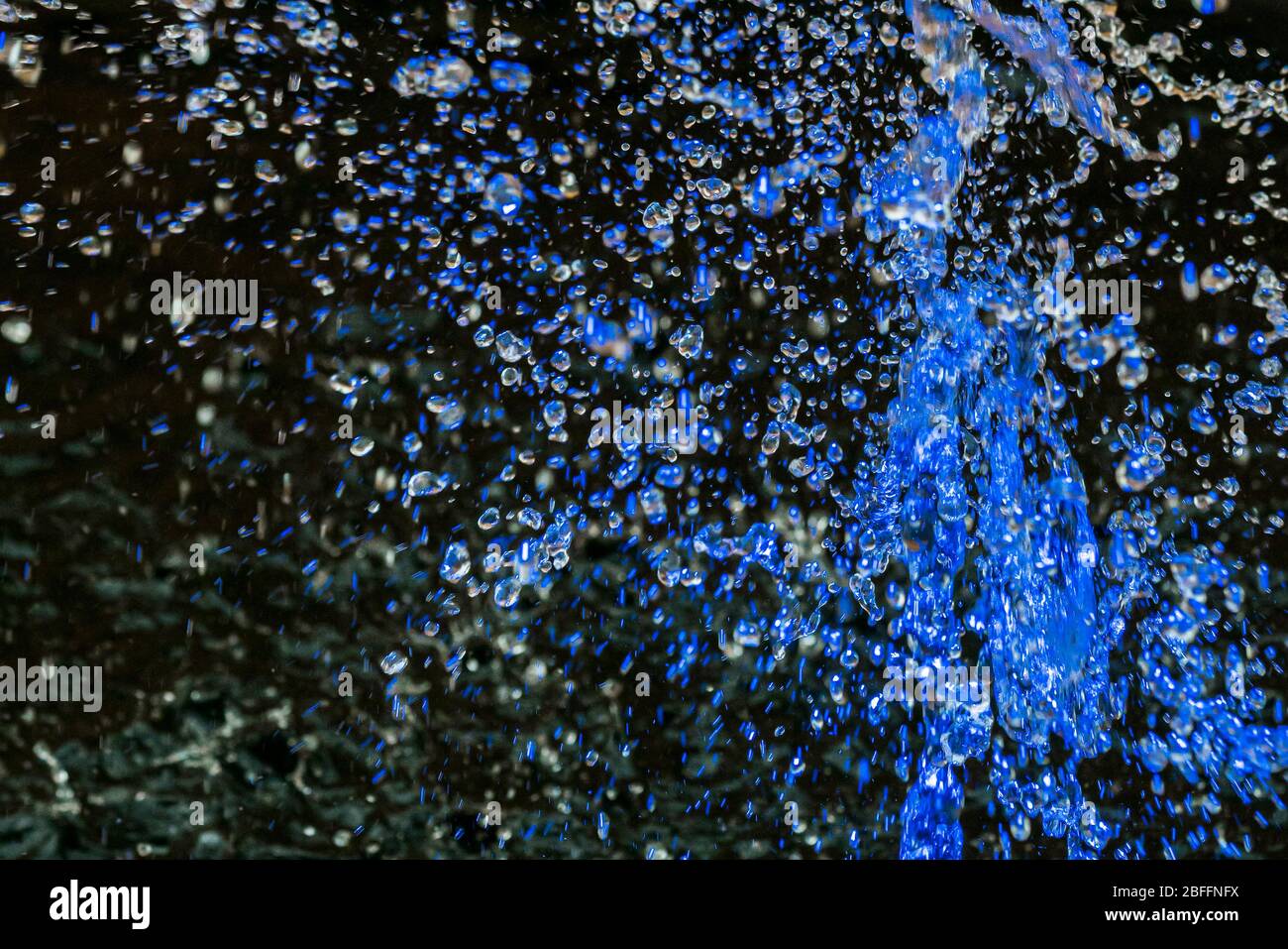 Primo piano di gocce d'acqua blu catturate a metà aria sopra una fontana su uno sfondo scuro Foto Stock