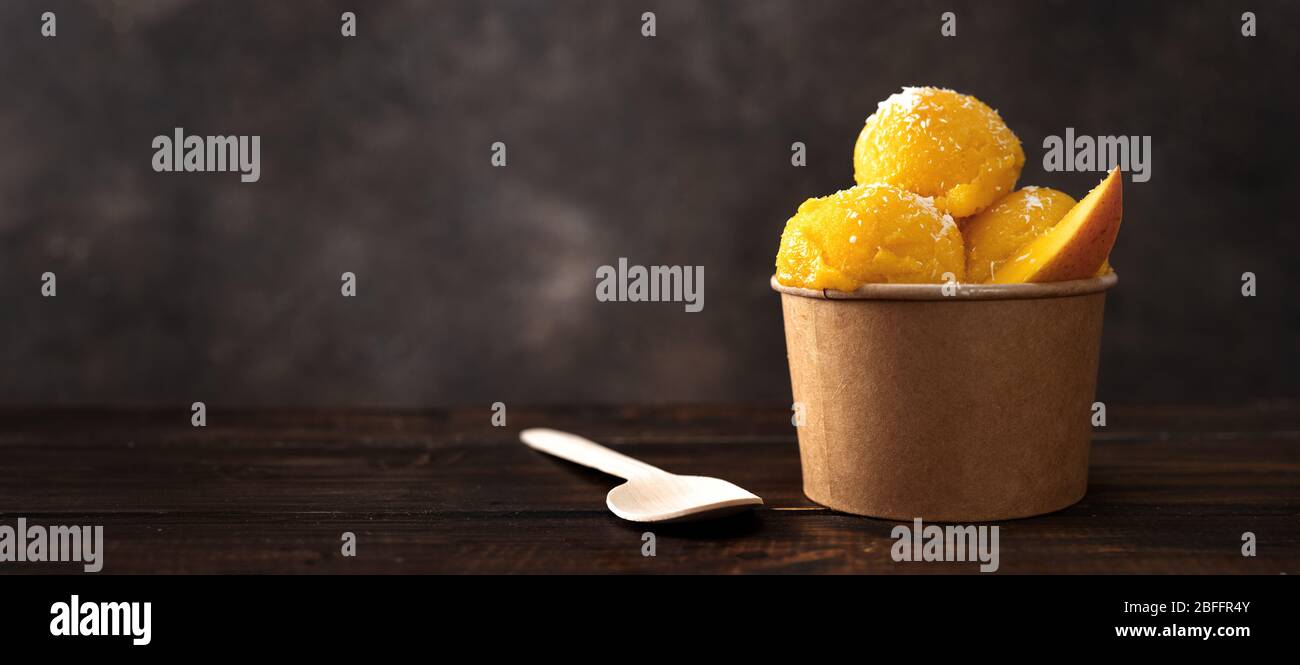 Sorbetto al mango in una tazza di carta artigianale con cucchiaio di legno Foto Stock