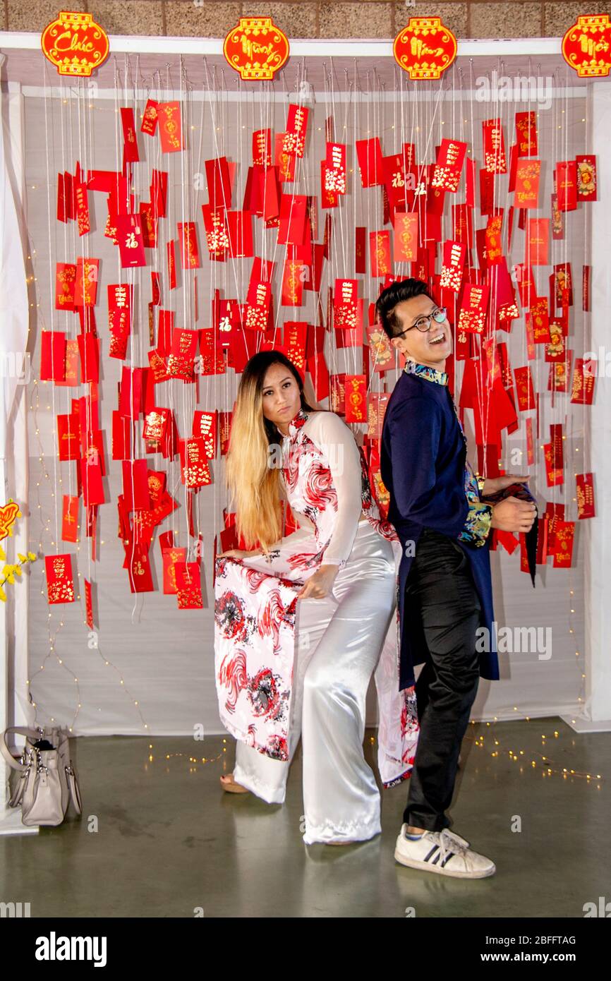 Una giovane coppia vietnamita americana posa in abbigliamento tradizionale asiatico in un colorato santuario con Lunar Capodanno o Tet tag e segni destinati a portare buona fortuna nel prossimo anno a una celebrazione a Costa Mesa, CA. Foto Stock