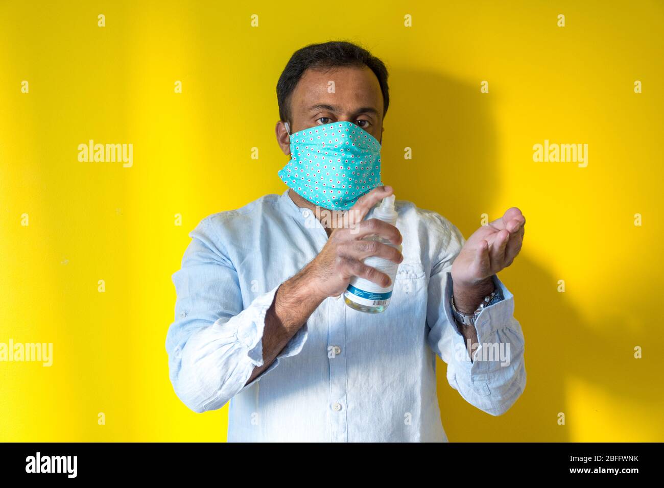 Modello maschio indossato in casa maschera facciale per evitare infezioni da virus corona durante la pandemia corona . Covid19, e spruzzando un igienizzante alla mano sinistra, Foto Stock