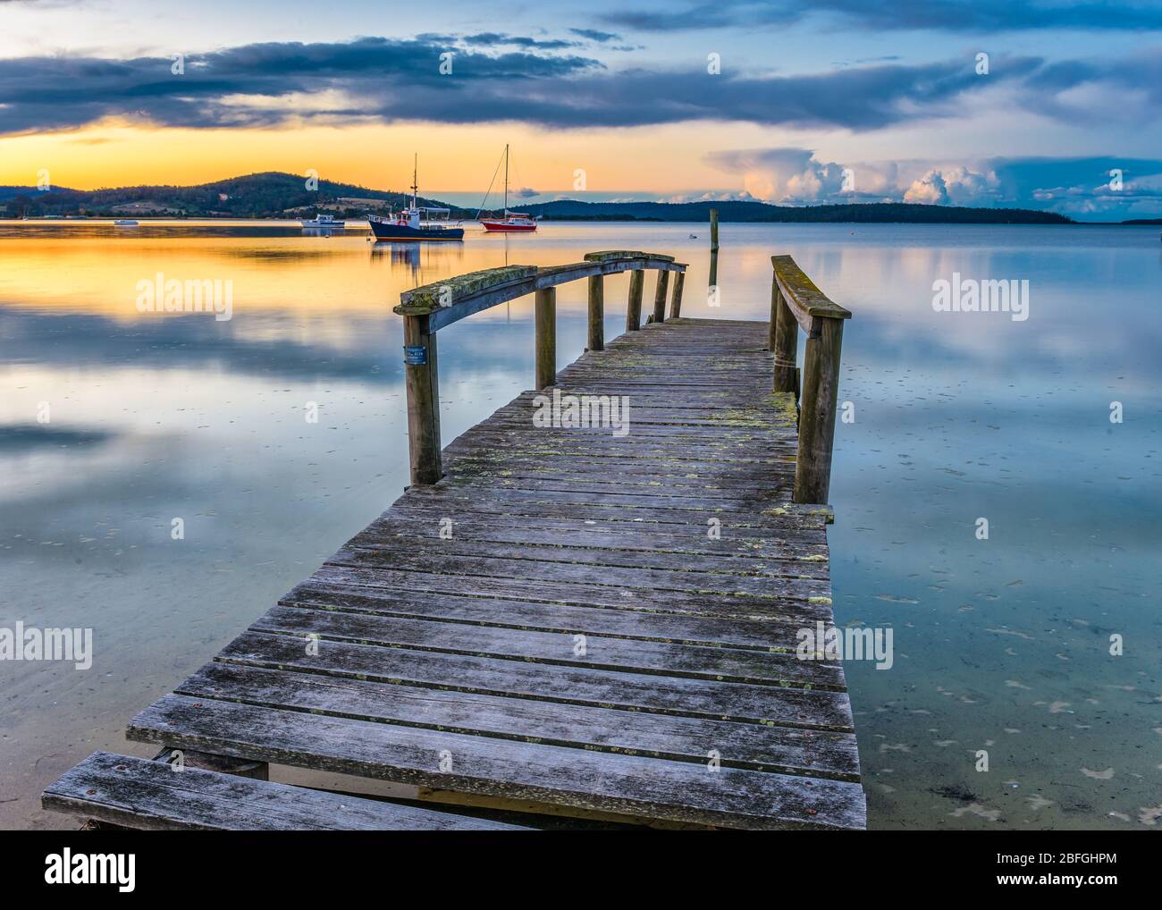 Un vecchio molo in legno e barche ormeggiate in modo sicuro si aggiungono al tramonto panoramico sulla superficie speculare della Baia di Sant''Elena in Tasmania. Foto Stock