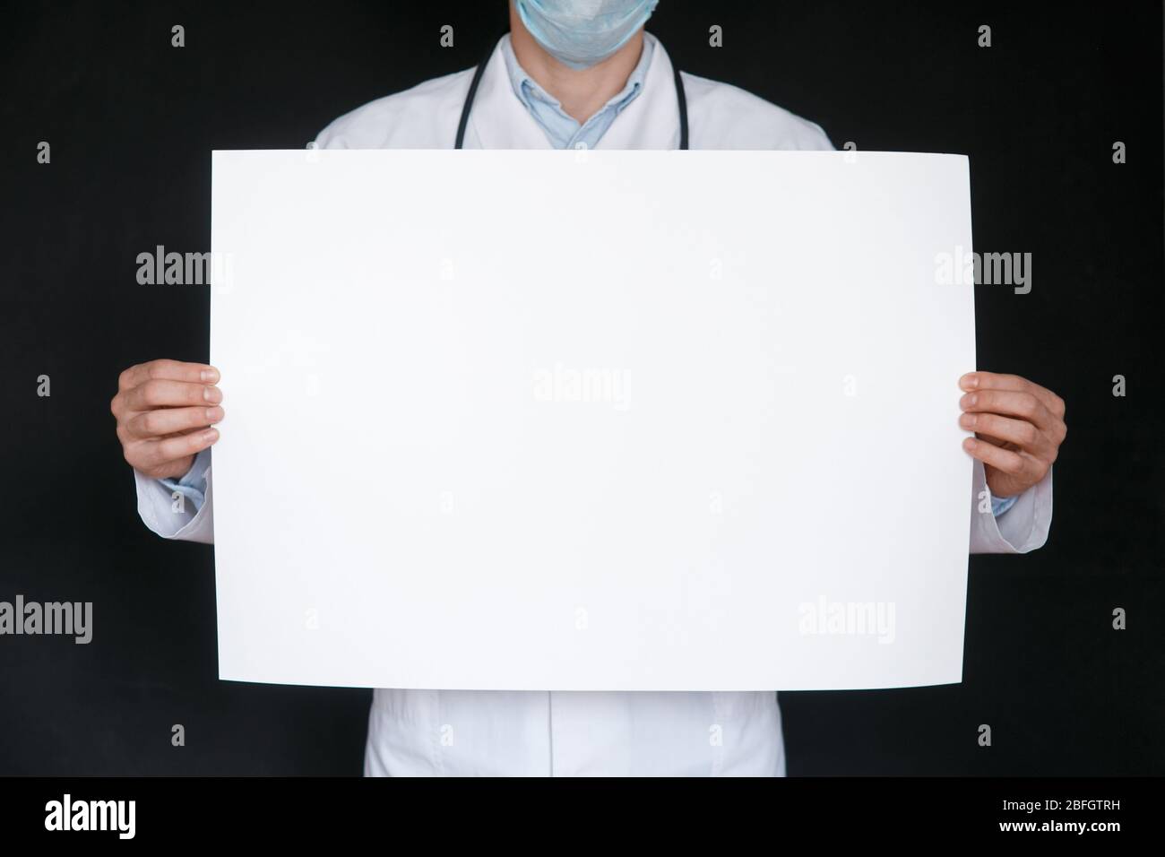 Un uomo in una t-shirt nera e guanti medici tiene un foglio bianco di carta. Mockup. Coronavirus. Quarantena . Epidemia. Spazio di copia. Avvertenza. Mano del medico in guanto blu che tiene fogli di carta. Foto Stock