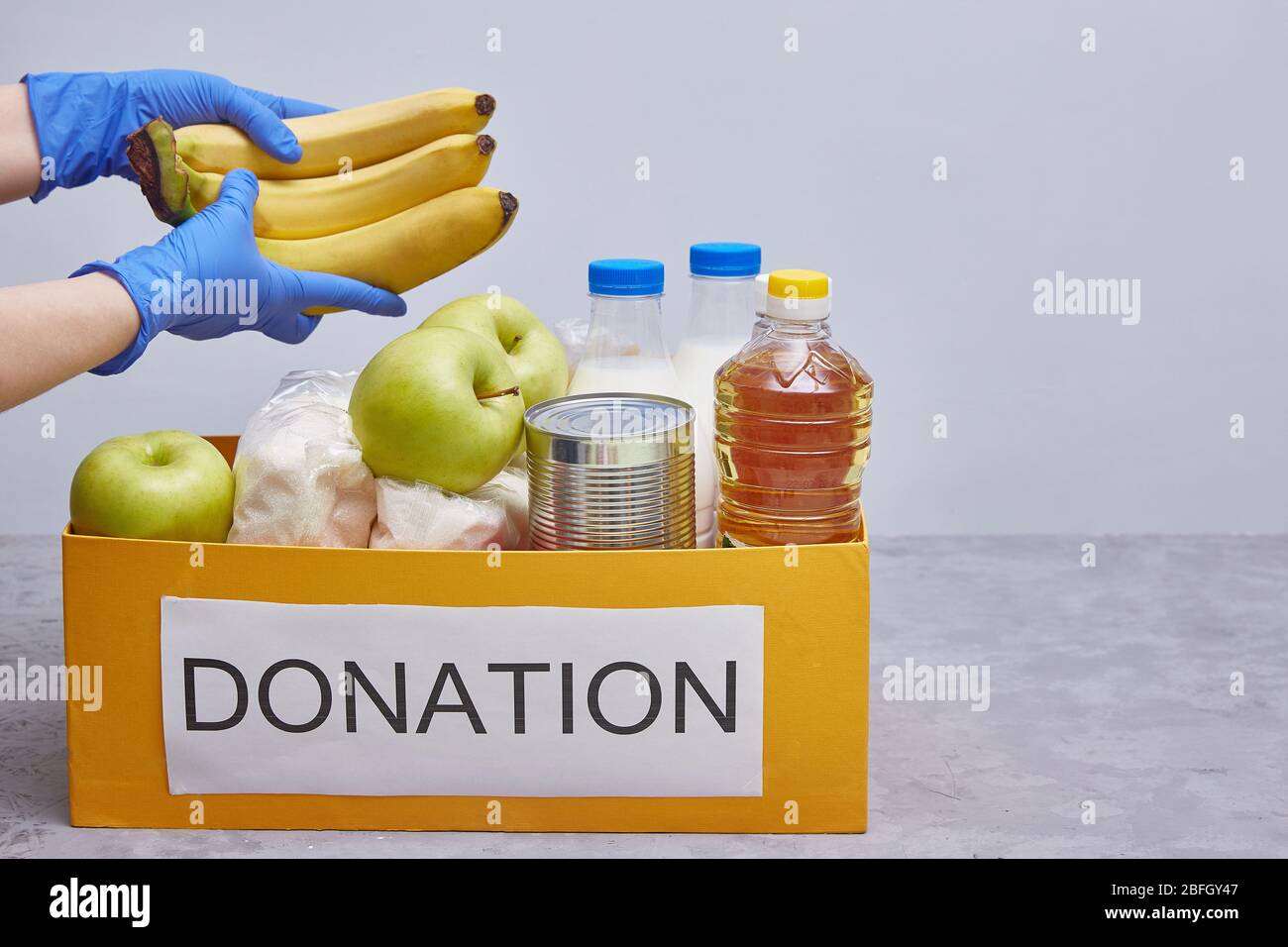 donazione e aiuto alimentare materiale durante la pandemia di coronavirus. Mani in guanti protettivi blu prendere o posare il cibo. Spazio di copia, senza volto. Foto Stock