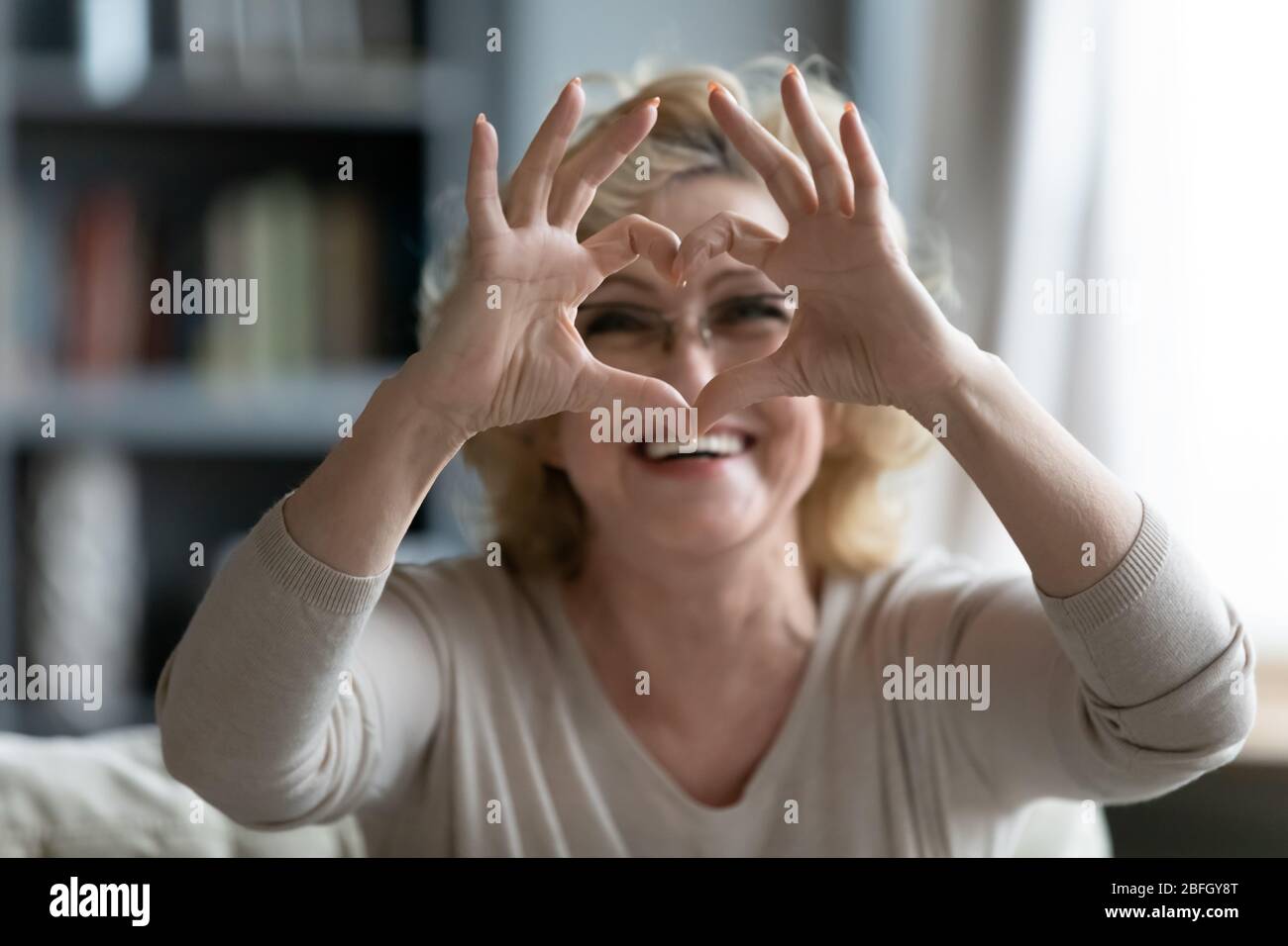 Donna anziana seduta sul divano con simbolo del cuore con le dita Foto Stock