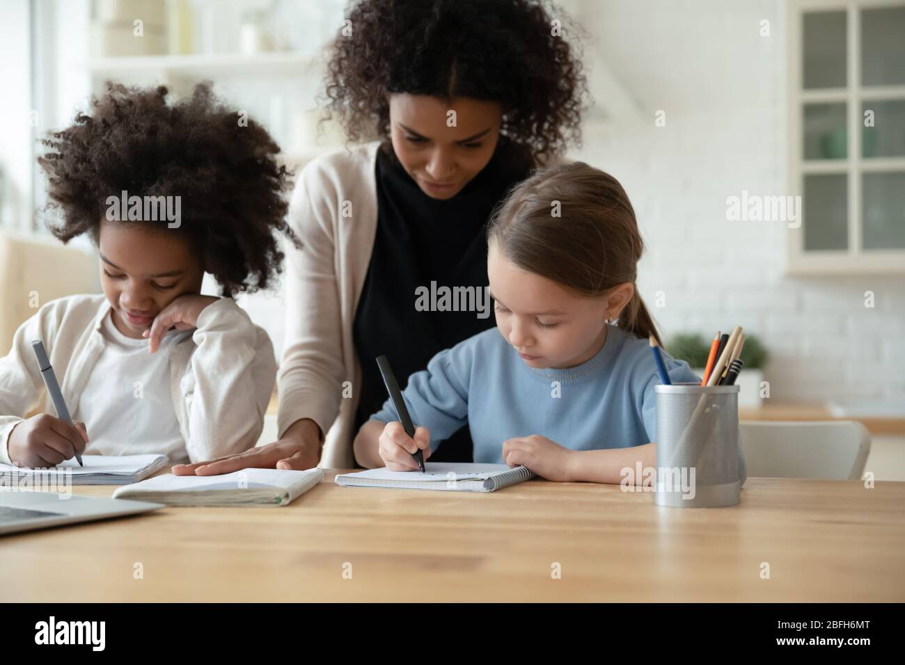 Mamma biraciale aiutare le ragazze multietniche con lezione online Foto Stock