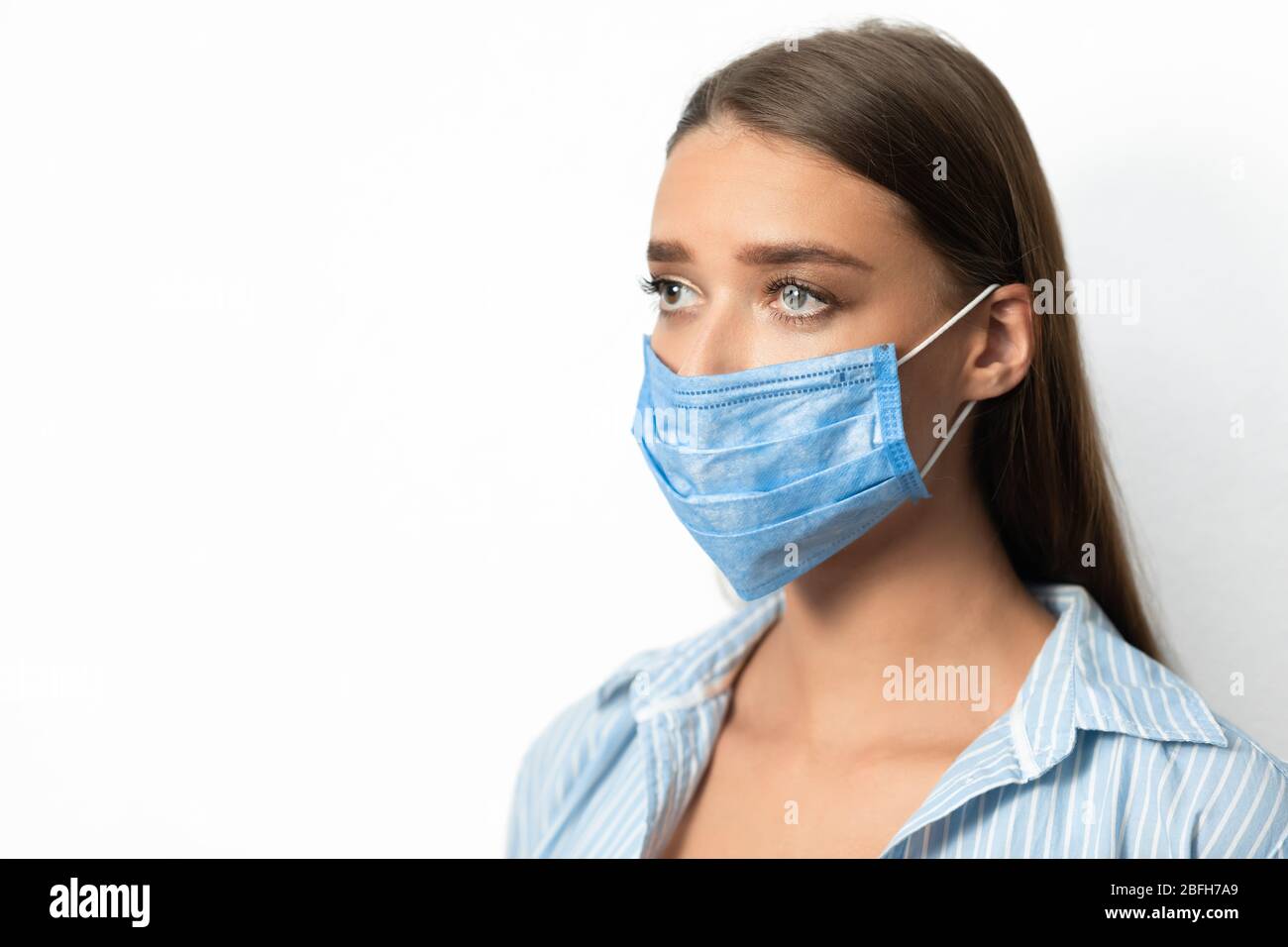 Donna malata che indossa maschera viso guardando da parte su sfondo bianco Foto Stock