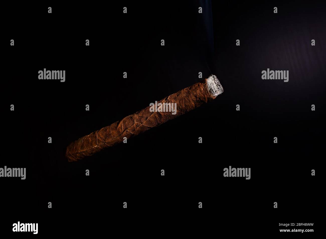Un sigaro cubano acceso fumando su uno sfondo nero Foto Stock