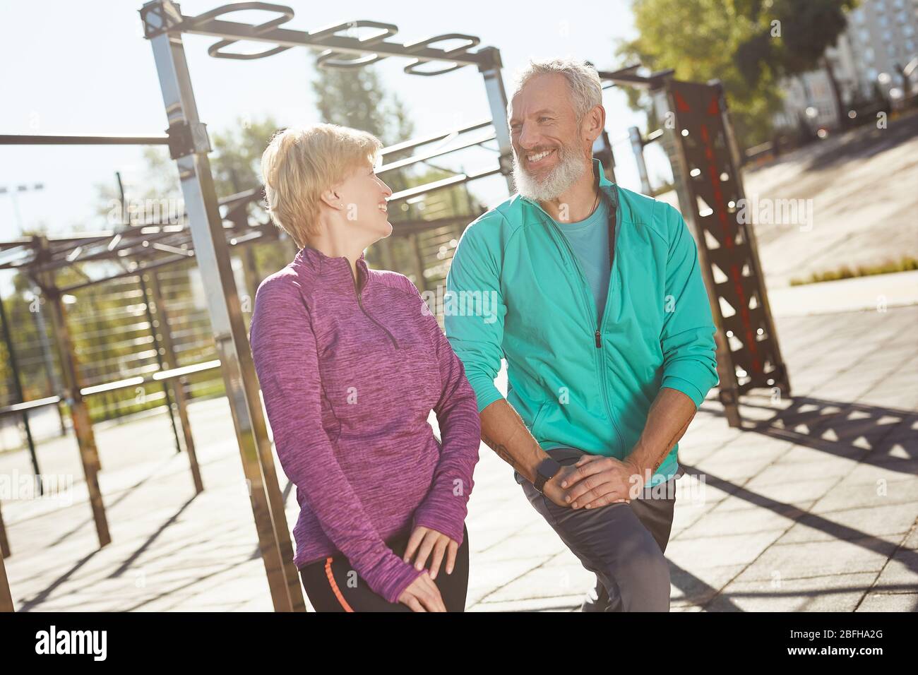 Riscaldamento. Felice coppia matura in famiglia in abbigliamento sportivo facendo ginnastica insieme allo stadio. Uomo e donna che fanno esercizi di stretching all'aperto Foto Stock