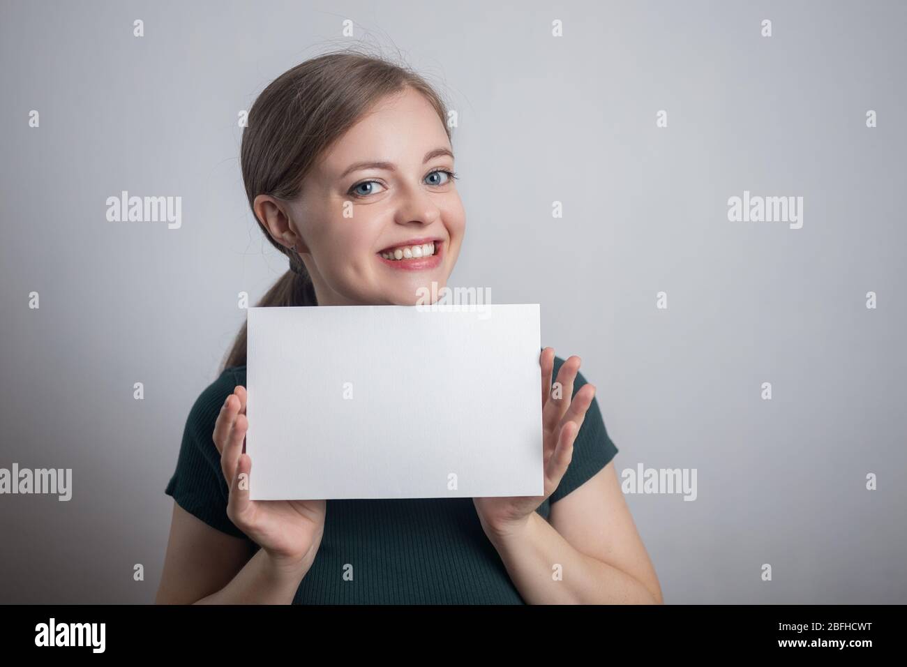 Sorridente giovane donna caucasica ragazza tenendo bianco foglio di carta con spazio per le copie Foto Stock