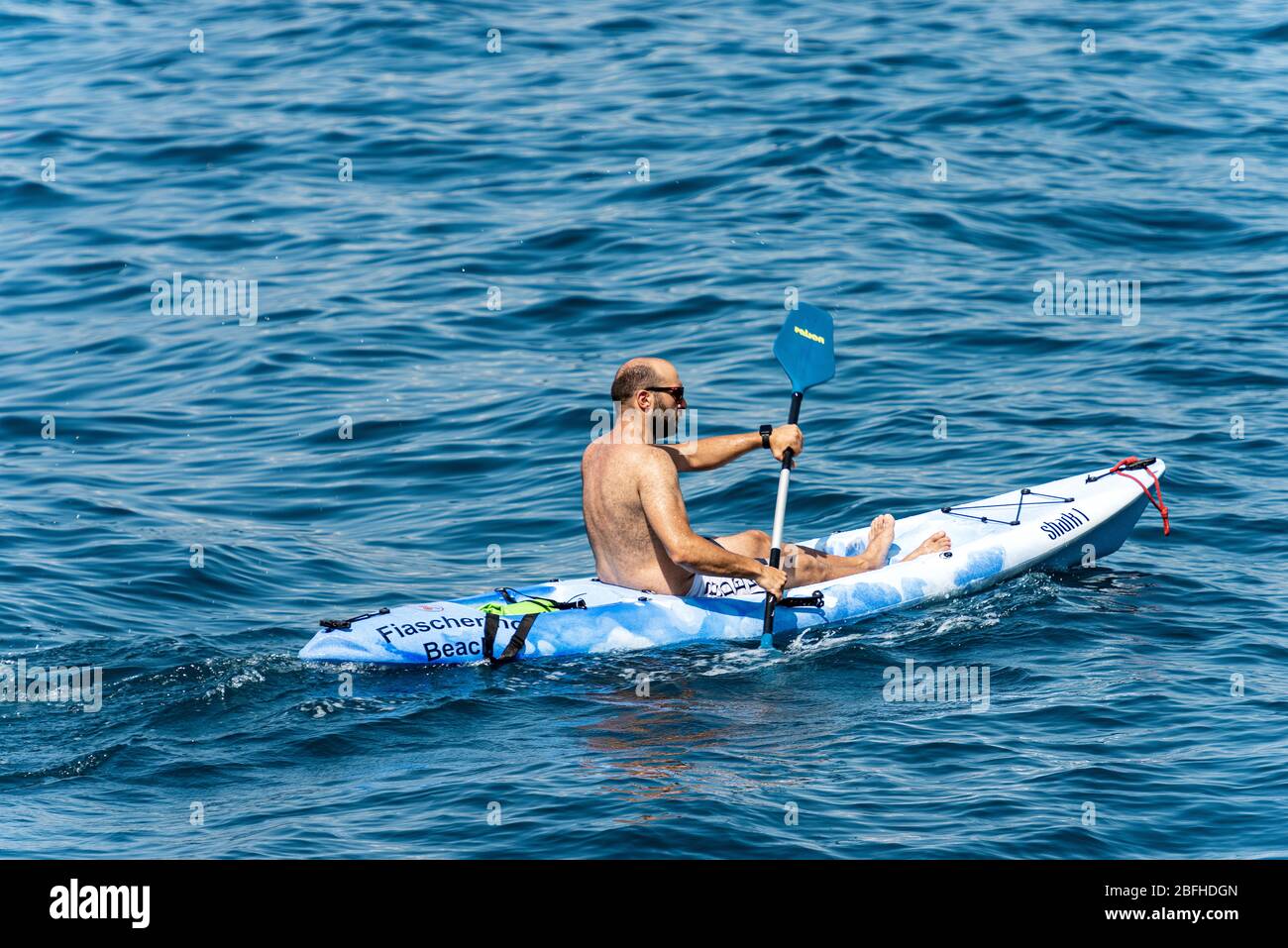 Kayak maschile in costume da bagno, pagaia nel blu del Mediterraneo. Golfo di la Spezia, Liguria, Italia, Europa Foto Stock