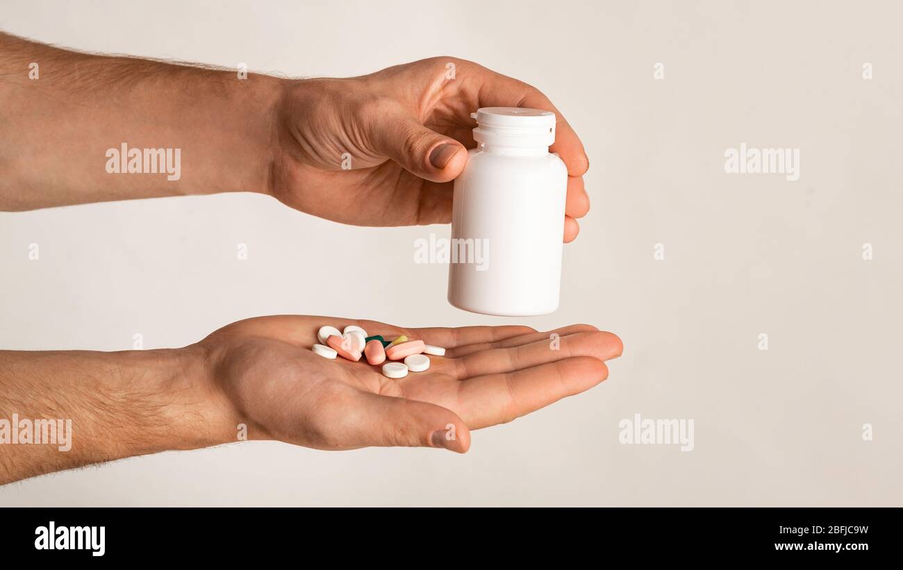 Ragazzo irriconoscibile che tiene bottiglia di meds e diverse pillole su sfondo chiaro, spazio per il design. Panorama Foto Stock