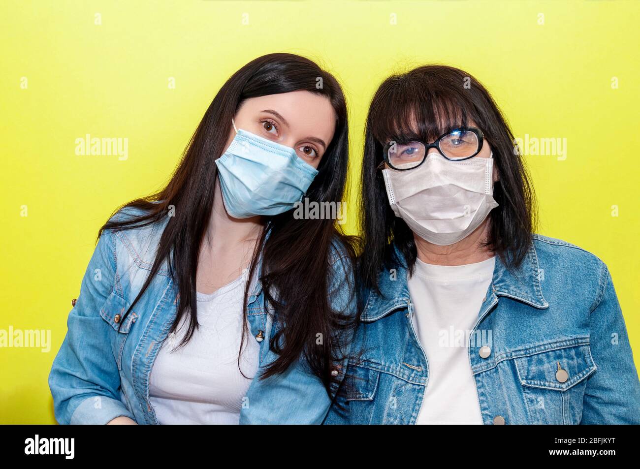 COVID-19. Madre e figlia in maschera protettiva viso medico su sfondo giallo. Concetto anti-Coronavirus. Foto Stock