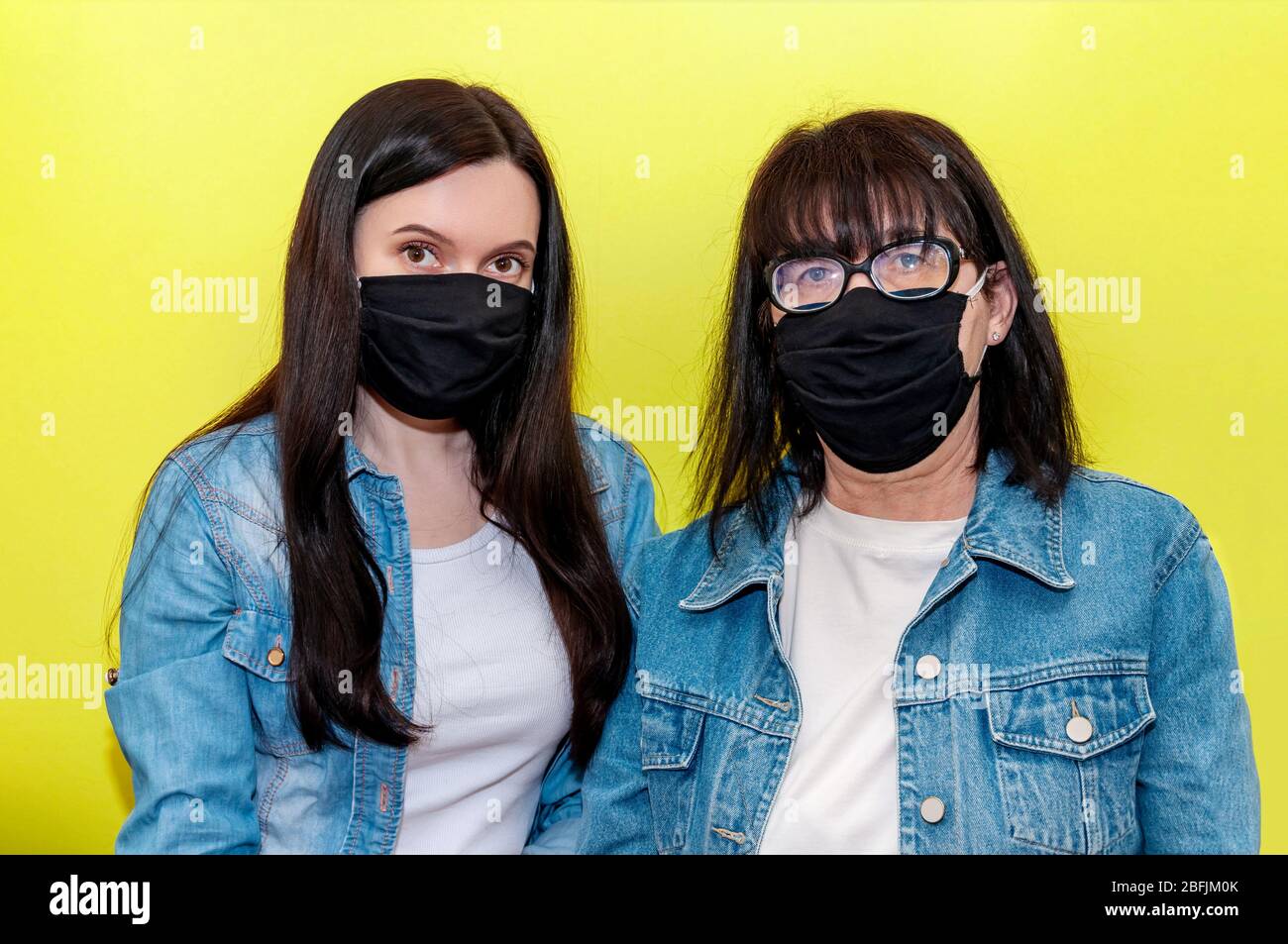 COVID-19. Madre e figlia in maschera protettiva viso medico su sfondo giallo. Concetto anti-Coronavirus. Foto Stock